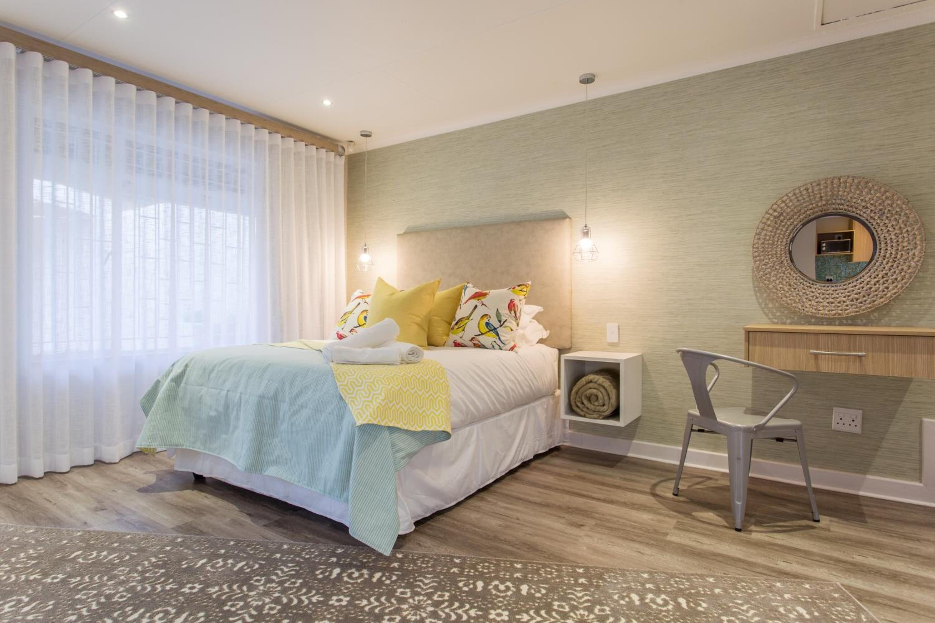 Un dormitorio moderno con cama, mesita de noche, silla y espejo en la pared.