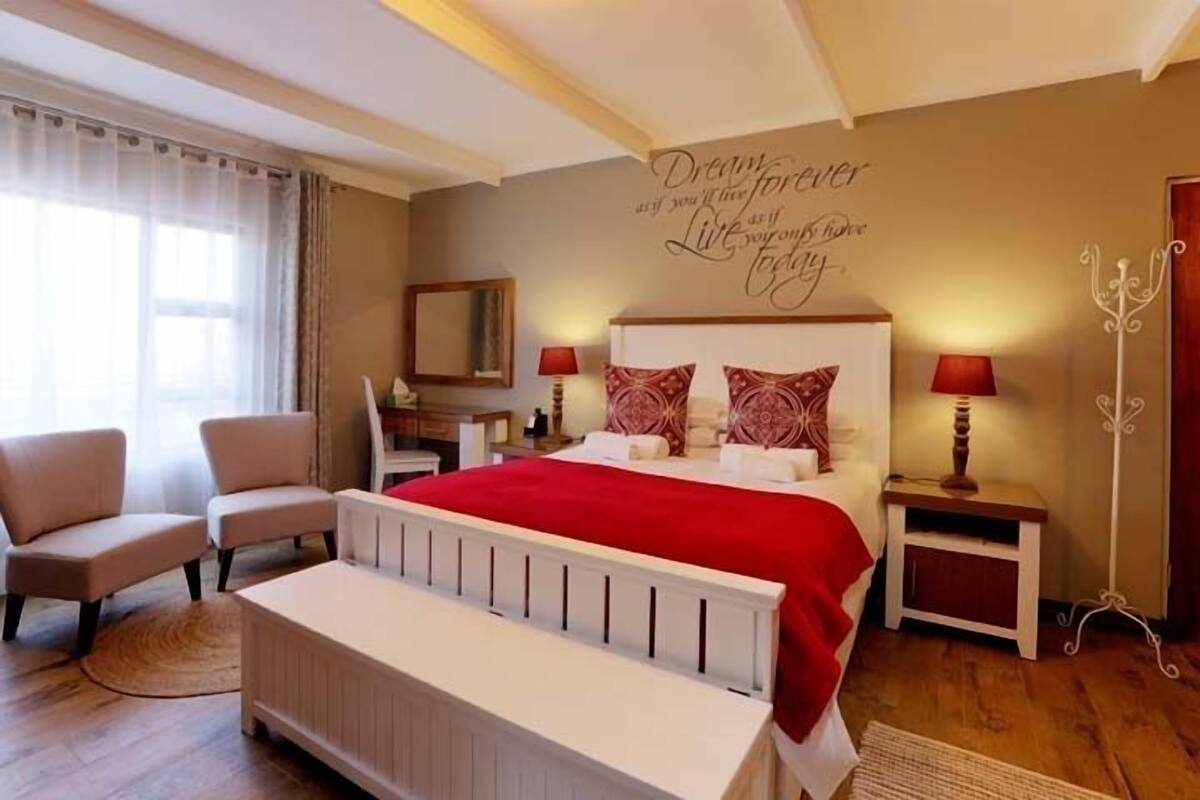 Een slaapkamer met een bed, twee nachtkastjes, een stoel, een spiegel en een muur met motiverende tekst.