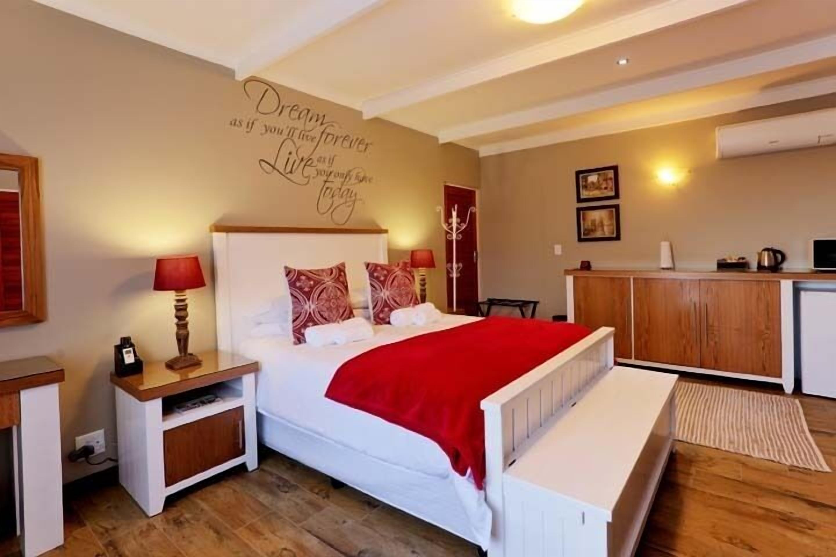 Una camera da letto con un letto, comodini, una coperta rossa, un muro con testo motivazionale e un angolo cottura.