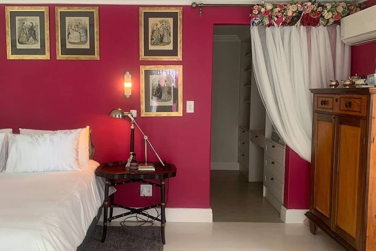A bedroom with a bed, a nightstand with a lamp, a dresser, and a door leading to another room.