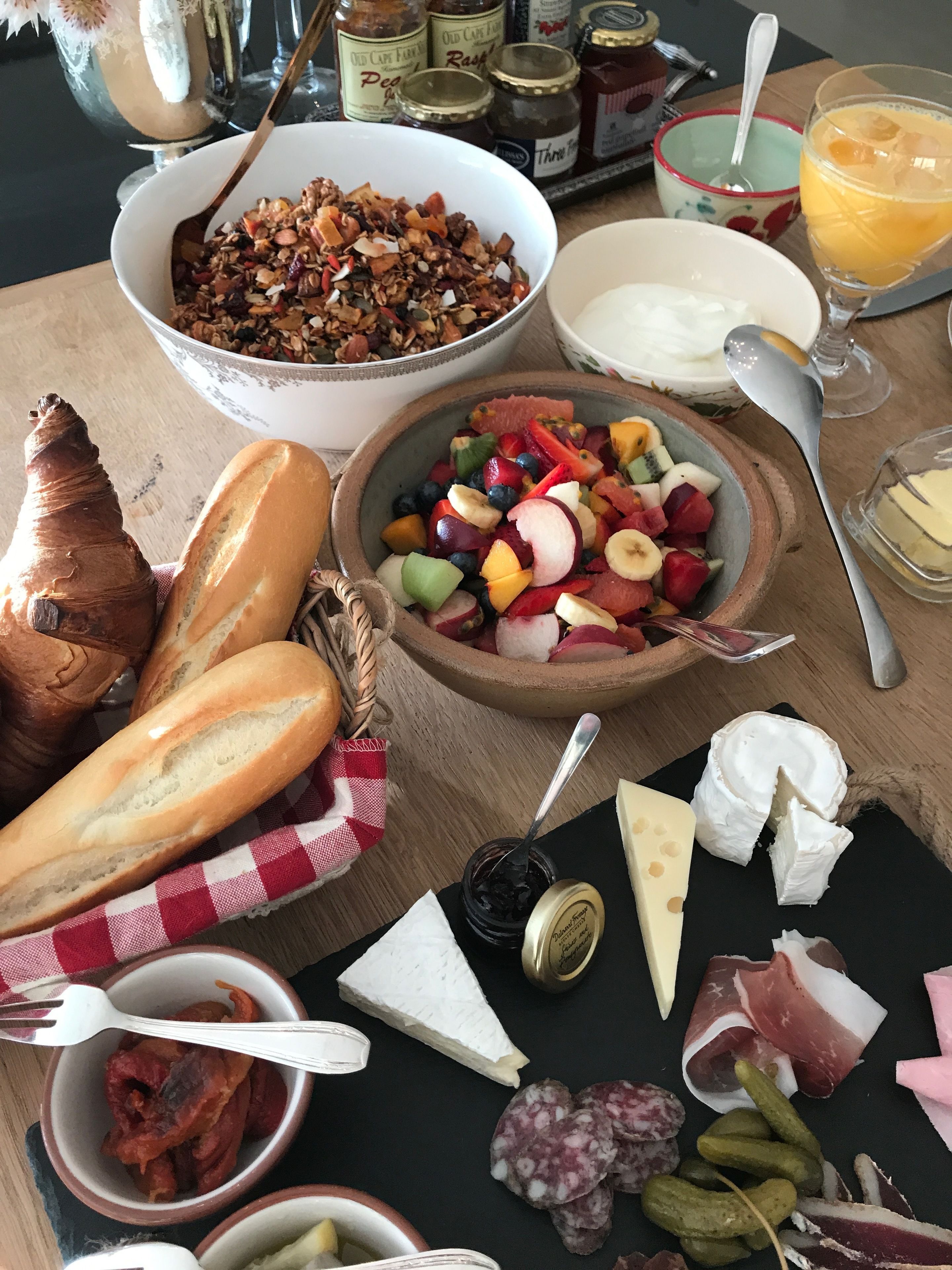 Uma mesa com diversos alimentos, como pão, queijo, embutidos e salada de frutas.