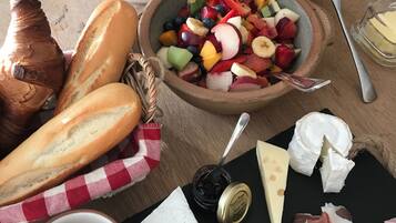 Uma mesa com diversos alimentos, como pão, queijo, embutidos e salada de frutas.