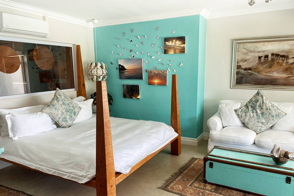 A bedroom with a four-poster bed, a white sofa, and a turquoise suitcase.