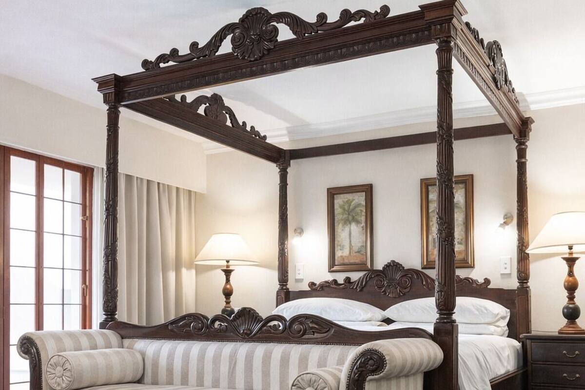 Un lit à baldaquin à quatre poteaux, agrémenté d’un canapé à rayures et d’un revêtement en tissu, d’une table de chevet en bois et de deux lampes fixées au mur.