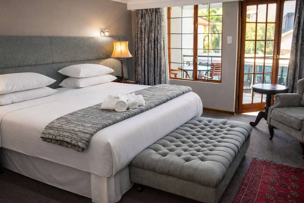 Une chambre d’hôtel avec un grand lit, une lampe de chevet, une fenêtre avec des rideaux, une petite table et une chaise.