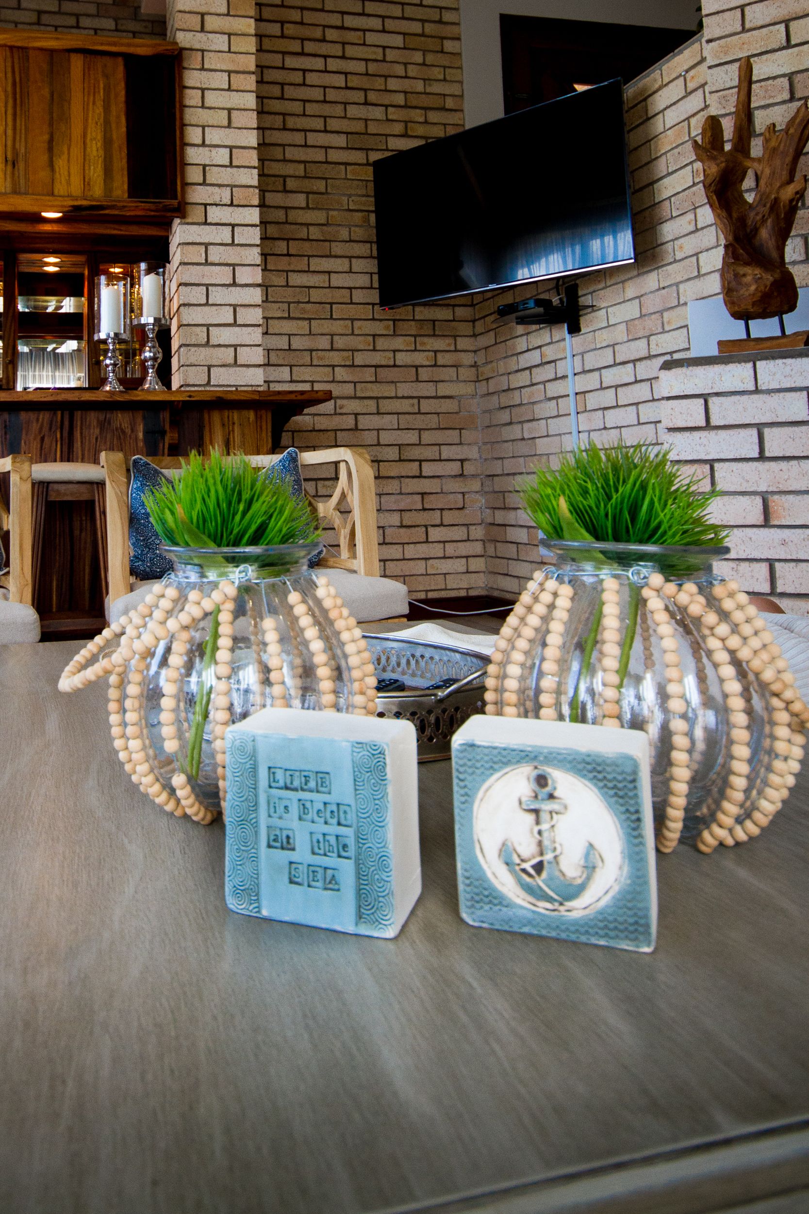 A living room with a brick wall, a flat-screen TV, and two decorative vases with green plants.