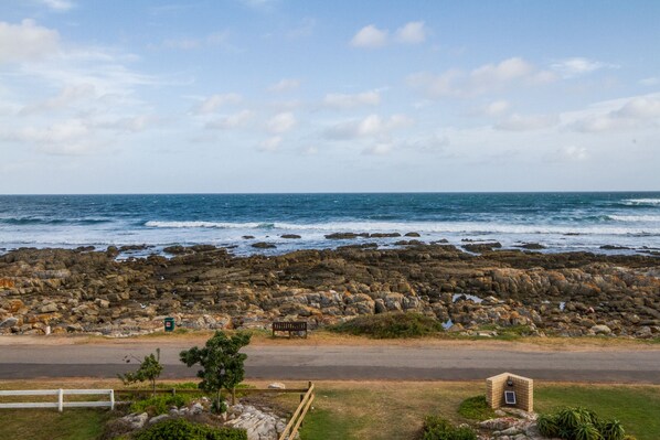 A rocky coastline with a bench and a small structure near the water. - Little Rock Guest House (Jongensfontein)