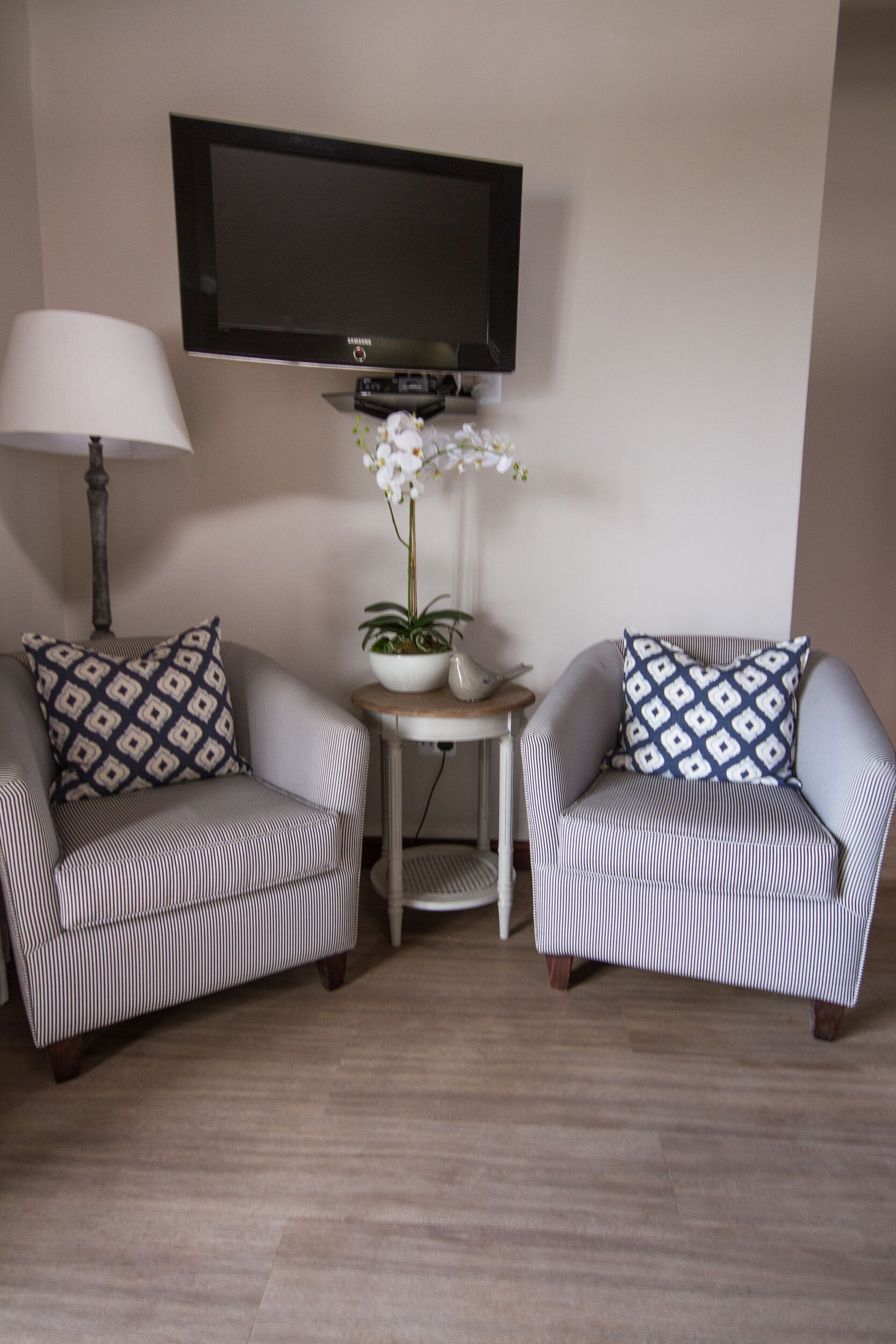 Two striped armchairs with patterned pillows, a small table with a potted plant, a lamp, and a flat-screen TV mounted on the wall.