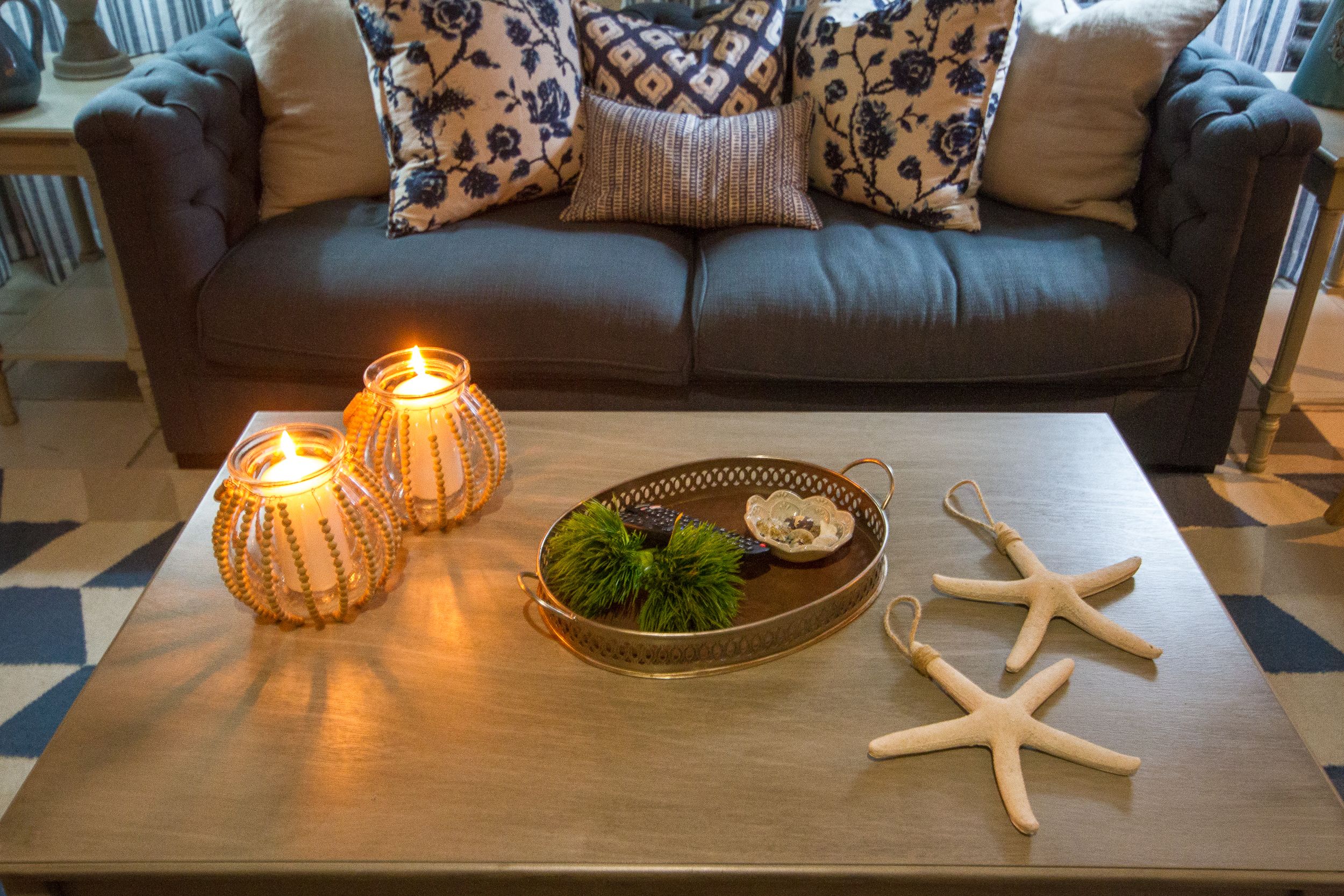 A cozy living room with a dark brown sofa adorned with patterned cushions, a wooden coffee table with decorative items including candles, a green plant, and starfish ornaments.