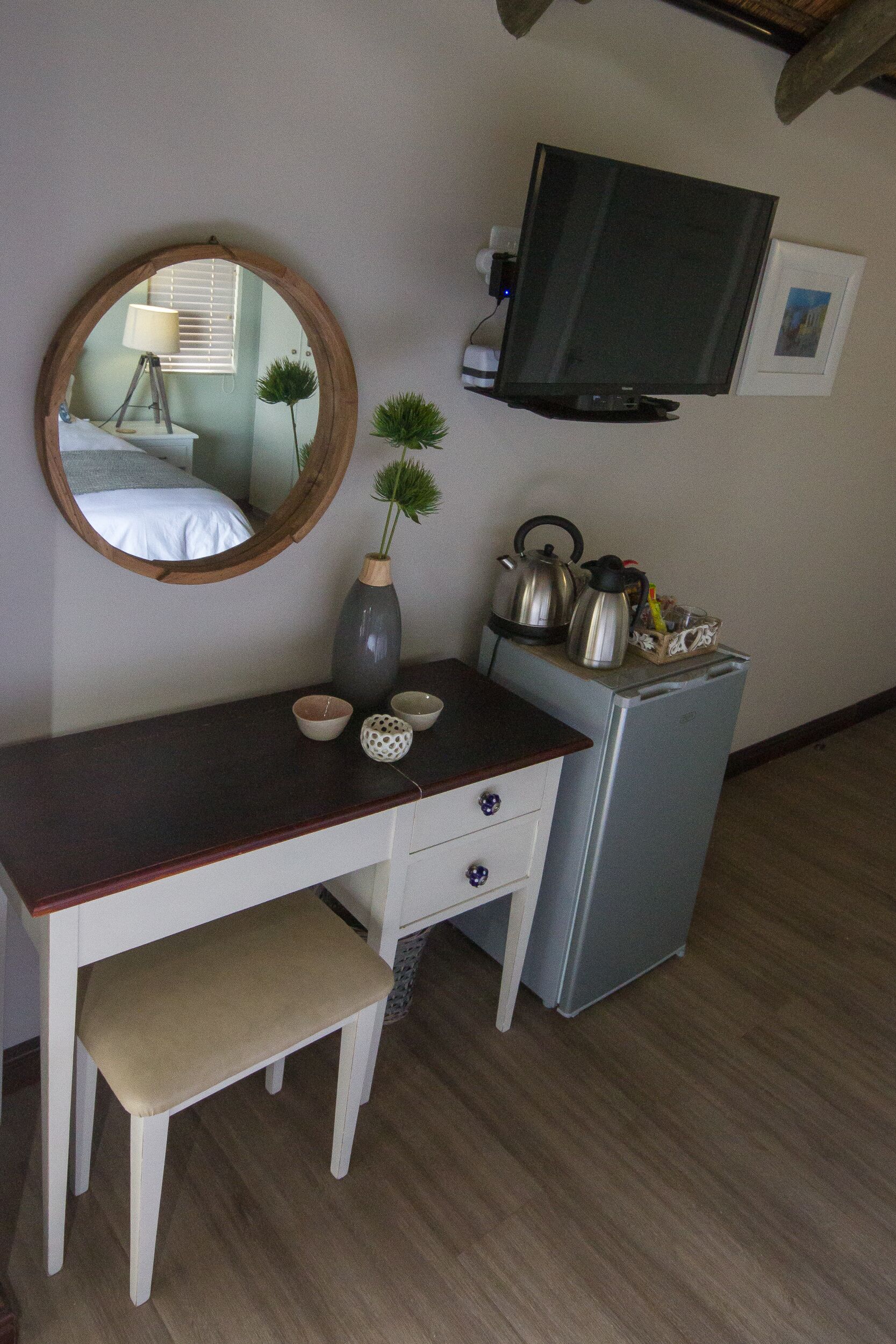 A small room with a wooden desk, a mirror, a television, and a refrigerator.