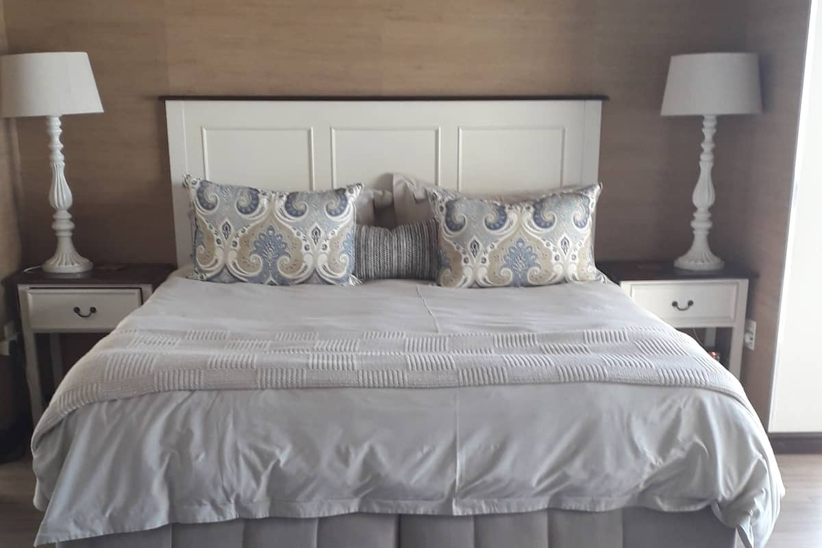 Un grand lit doté d’une tête de lit capitonnée, de deux tables de chevet et de coussins décoratifs.