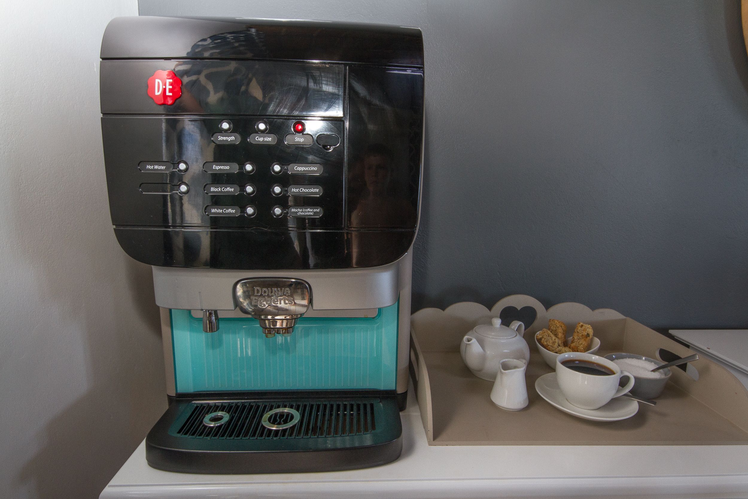 A coffee machine with various drink options on a tray with cups and pastries.