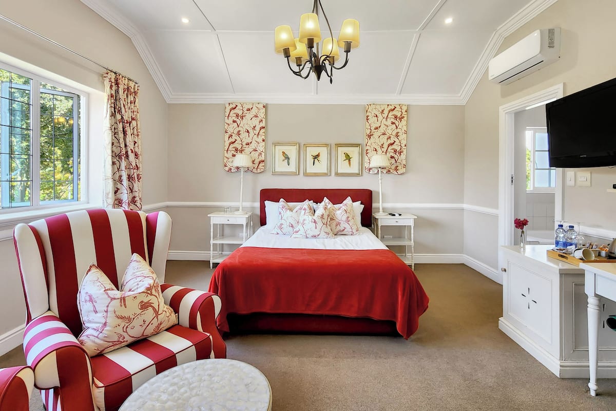 A bedroom with a large bed, a red and white striped chair, a chandelier, and a television.