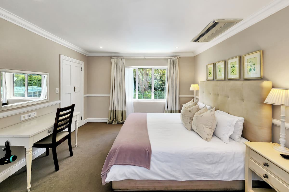 A bedroom with a bed, bedside table, lamp, desk, chair, and a window with curtains.