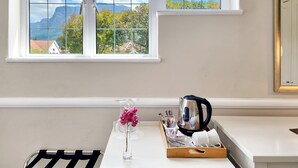 A room with a large window offering a mountain view, a white table with a vase of flowers, a kettle, and a tray with various items. - Roodenburg House 1882 (Cape Town)
