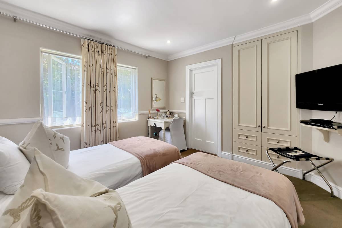 A hotel room with two beds, a vanity with a mirror, a television, and a window with curtains.