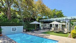 A swimming pool with tiled edges, surrounded by a patio area with outdoor furniture and a glass-enclosed structure. - Roodenburg House 1882 (Cape Town)
