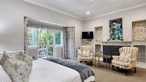 A spacious bedroom with a large bed, two armchairs, a television, and a fireplace. - Roodenburg House 1882 (Cape Town)