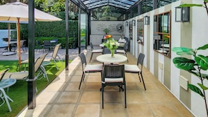 A covered patio area with a glass ceiling, outdoor seating, and a central table with chairs. - Roodenburg House 1882 (Cape Town)