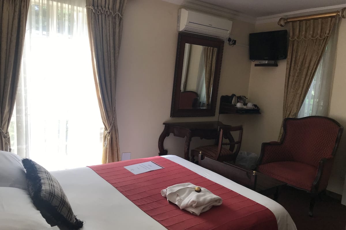 Una habitación de hotel con cama, una silla, un escritorio, aire acondicionado y televisor.