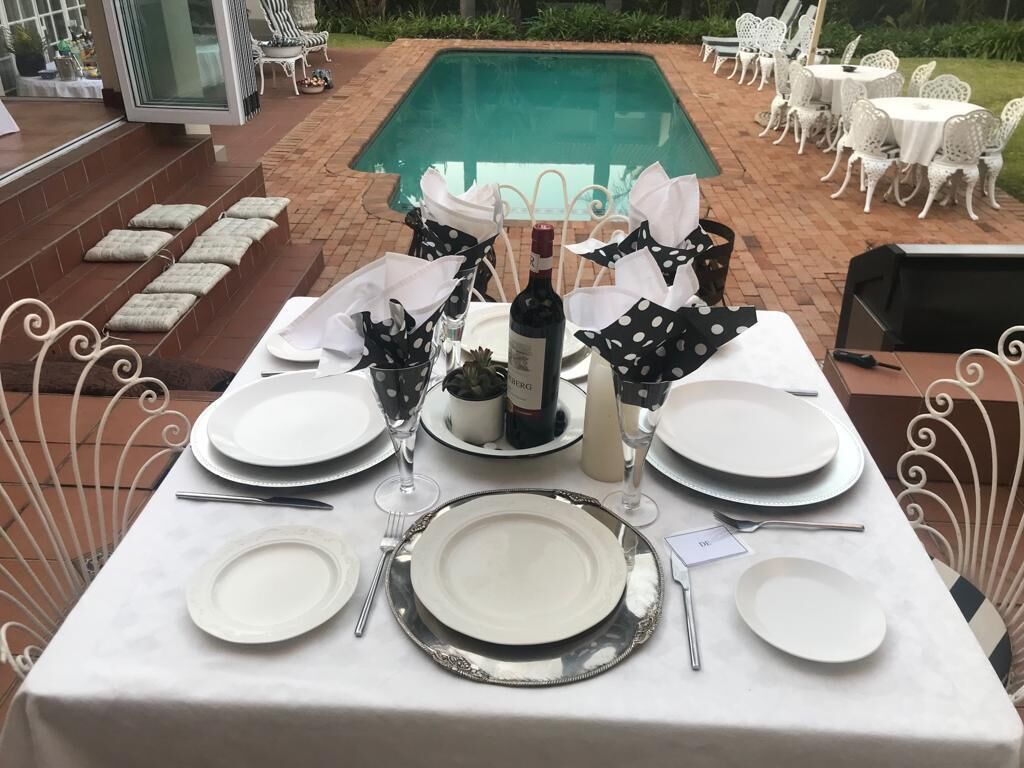 A table set for a meal with white plates, silverware, and a bottle of wine, surrounded by white chairs with black polka dot napkins.