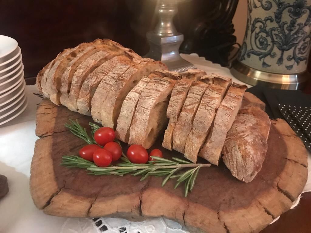 A loaf of sliced bread on a wooden board with cherry tomatoes and rosemary.
