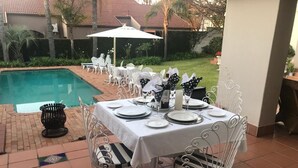 Un espace extérieur aménagé pour les repas, avec une piscine, des chaises en métal blanc et une table dressée pour un repas.