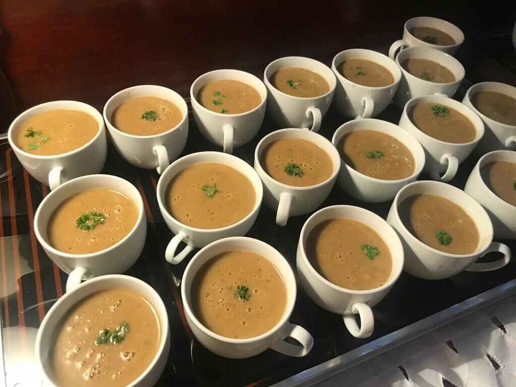 En bakke med hvide kopper fyldt med en brun drik, sandsynligvis kaffe, placeret på en reflekterende overflade.