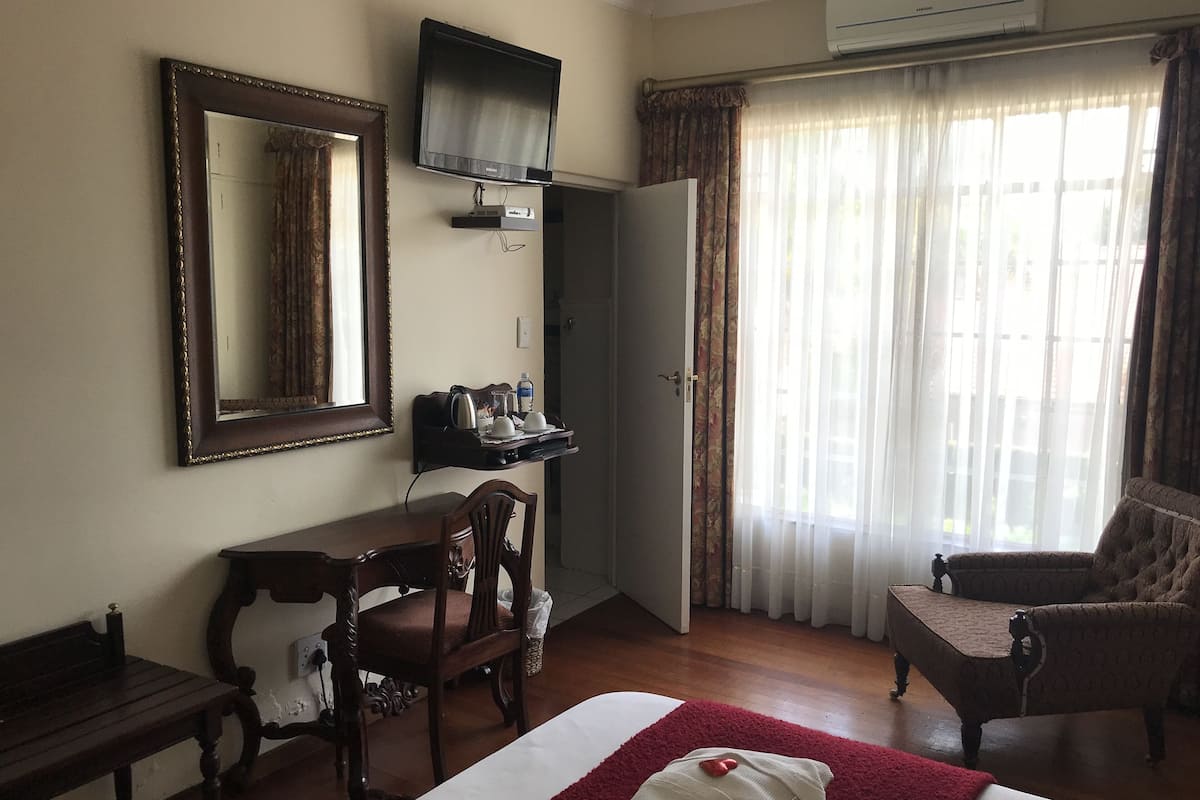 Una habitación de hotel con cama, escritorio, silla, televisión y ventana con cortinas.