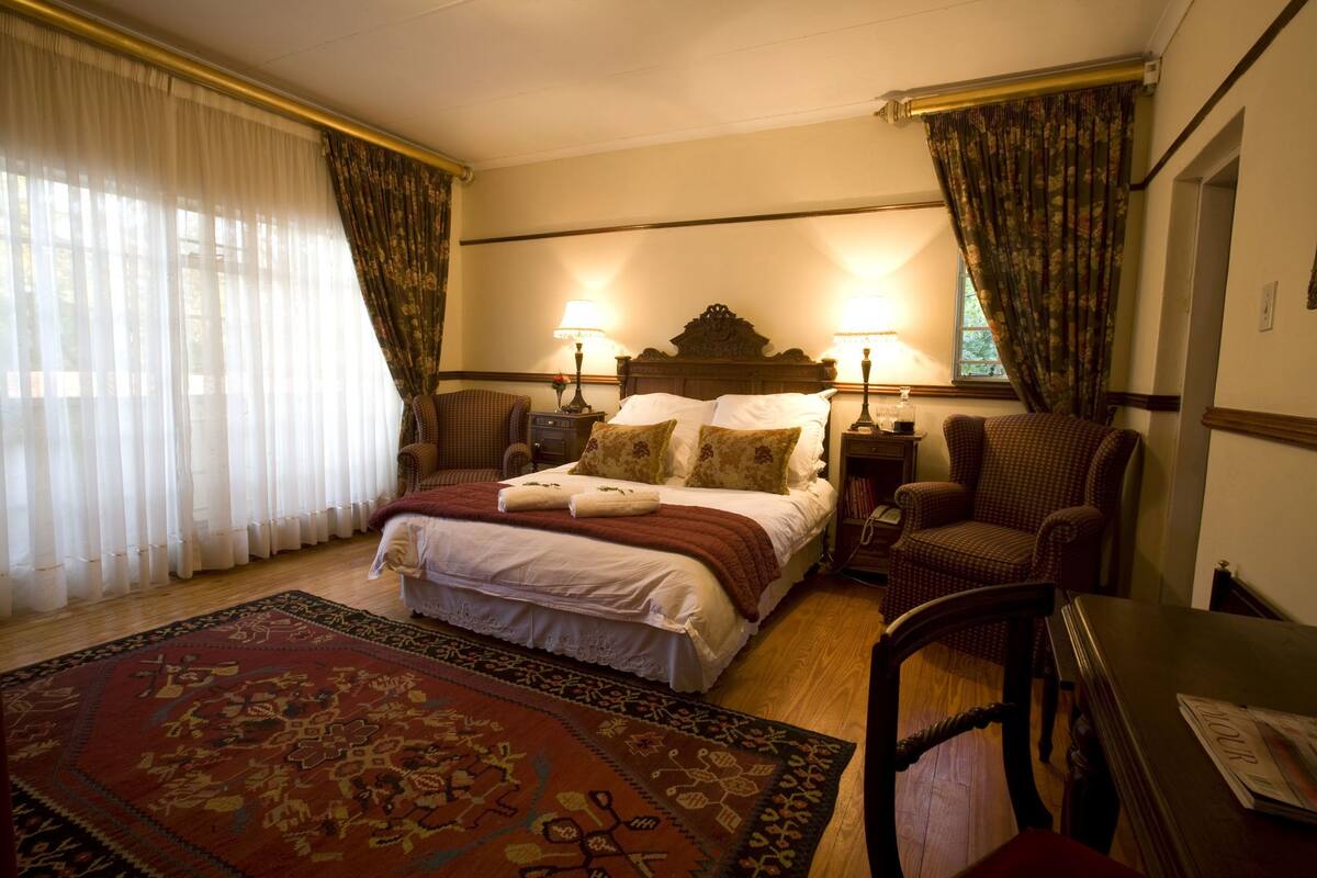 Habitación de hotel con una cama grande, dos lámparas de noche, una silla de madera, una mesa y un tapete estampado.
