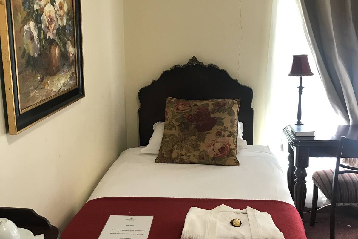 Una habitación de hotel con una cama, un cuadro, aire acondicionado, un escritorio y una silla.