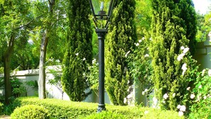 Un jardin bien entretenu, avec une variété d’arbres, des arbustes soigneusement taillés et un lampadaire central.
