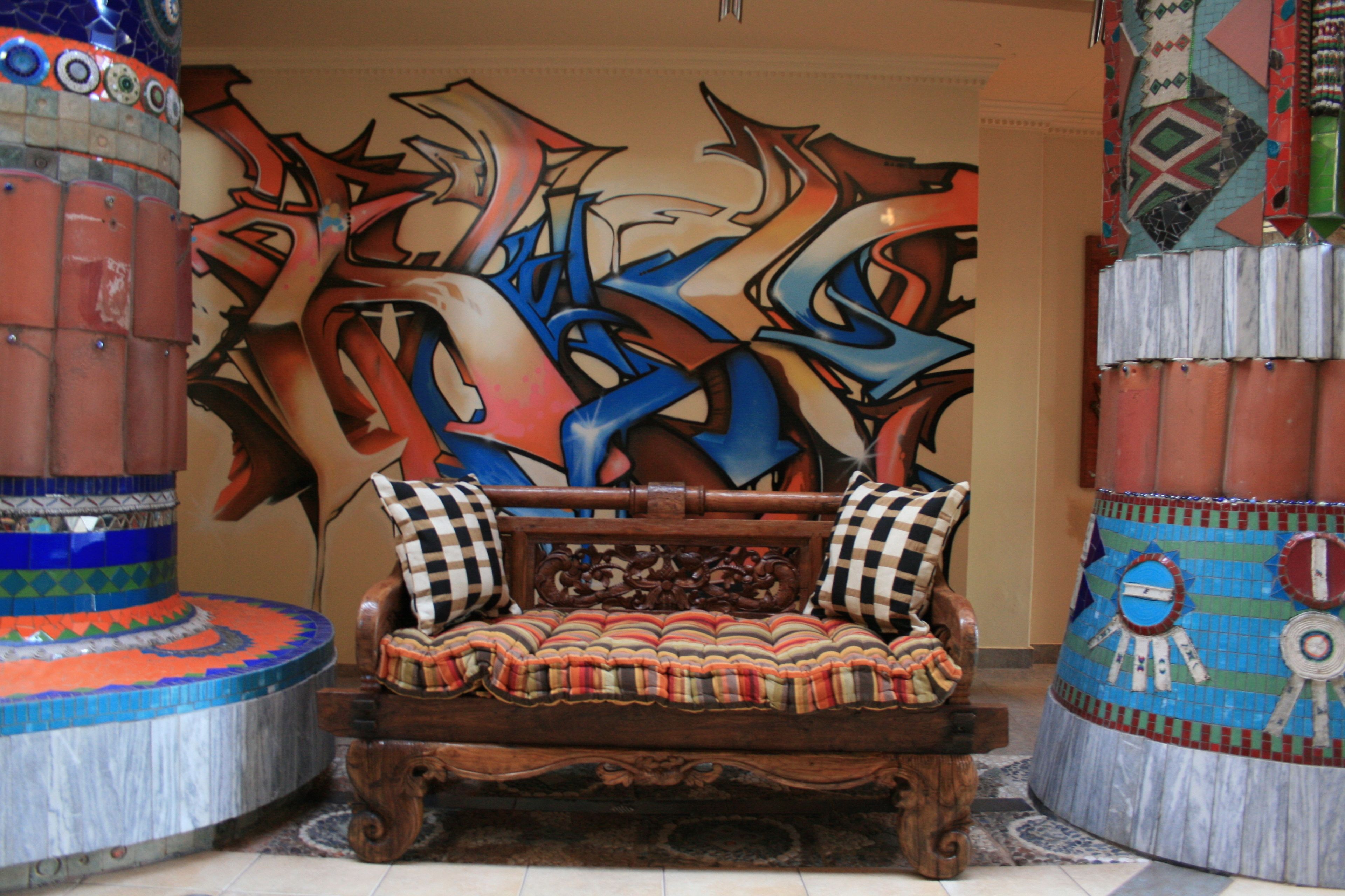 A wooden sofa with checkered cushions in a room with a large abstract mural on the wall.