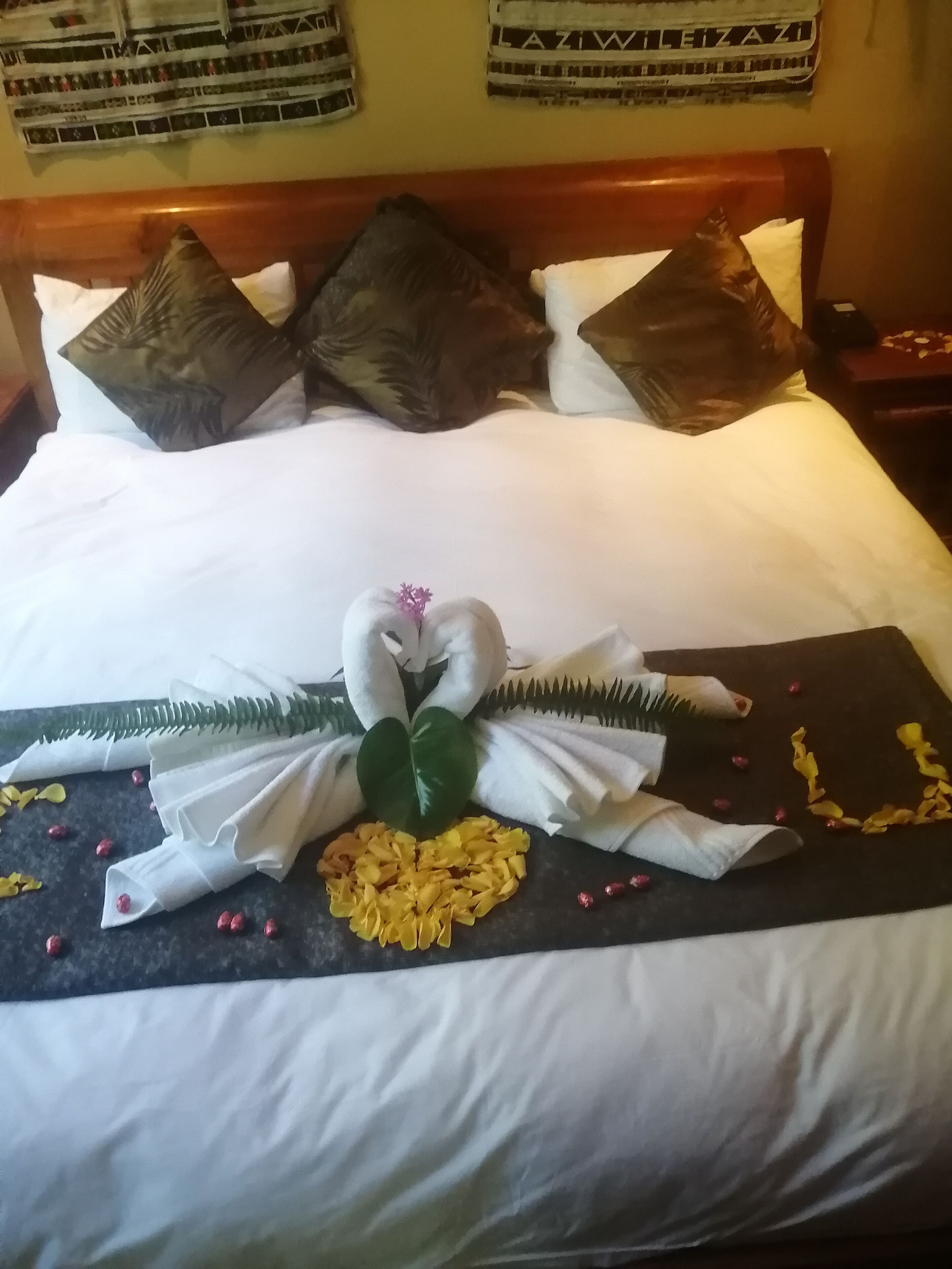 A neatly made bed with a decorative centerpiece featuring a swan and flowers, and a dark-colored throw blanket with yellow flowers and red berries.