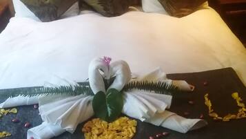 A neatly made bed with a decorative centerpiece featuring a swan and flowers, and a dark-colored throw blanket with yellow flowers and red berries.
