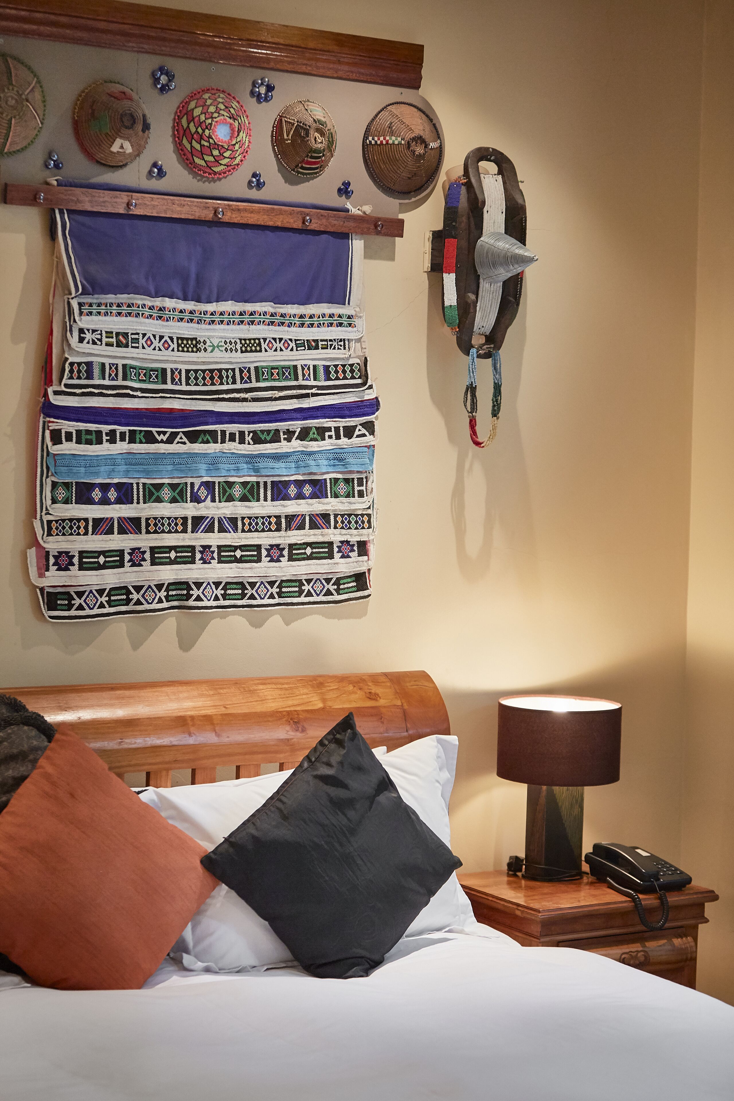 A neatly made bed with a wooden headboard, a bedside lamp, and a telephone on a wooden nightstand.