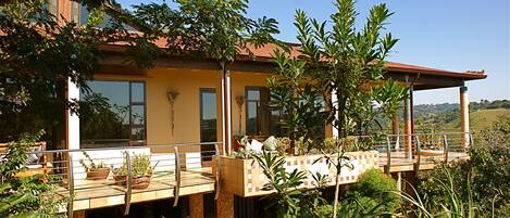 A two-story house with a balcony, large windows, and potted plants.