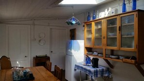 A kitchen with a wooden table, a refrigerator, and a cabinet with glass doors. - Bedrock Lodge (Port Nolloth)