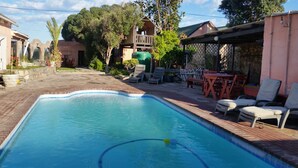 En swimmingpool med flisekant, omgivet af en patio med liggestole og et bord.