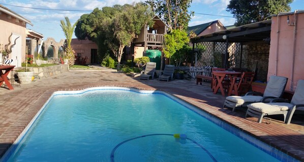 A swimming pool with a tiled edge, surrounded by a patio area with lounge chairs and a table. - Bedrock Lodge (Port Nolloth)