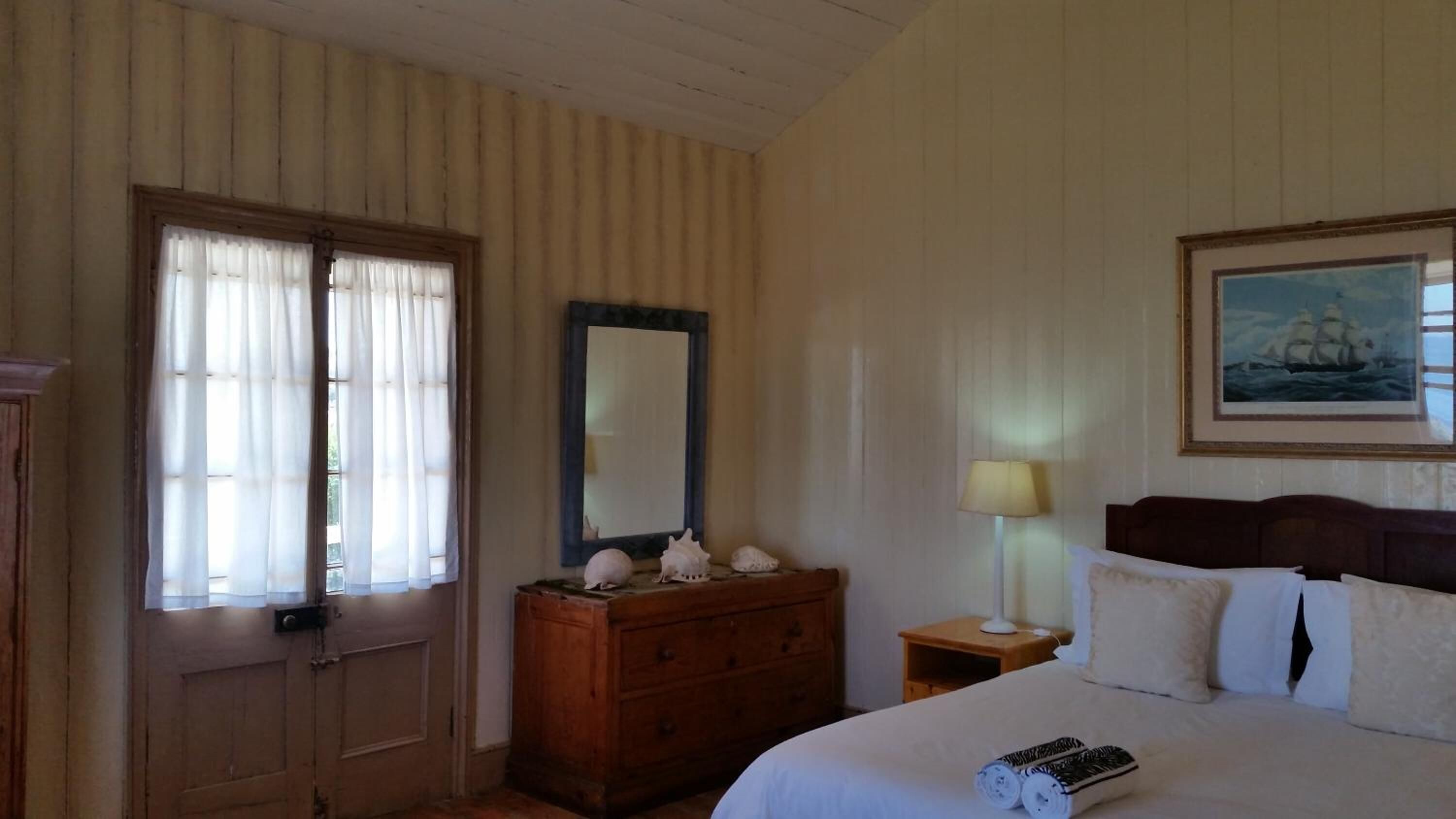A hotel room with a bed, a dresser, a mirror, a lamp, and a painting on the wall.