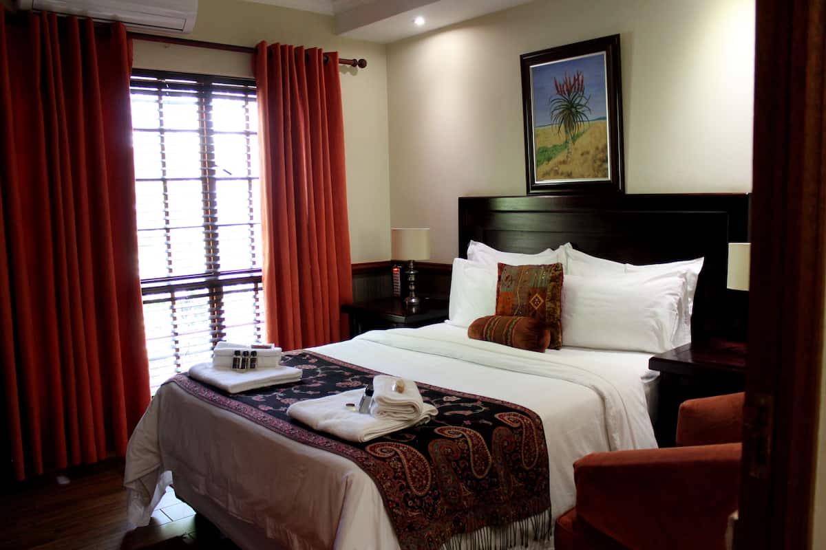 A hotel room with a bed, a nightstand, a lamp, a painting on the wall, and a window with curtains.
