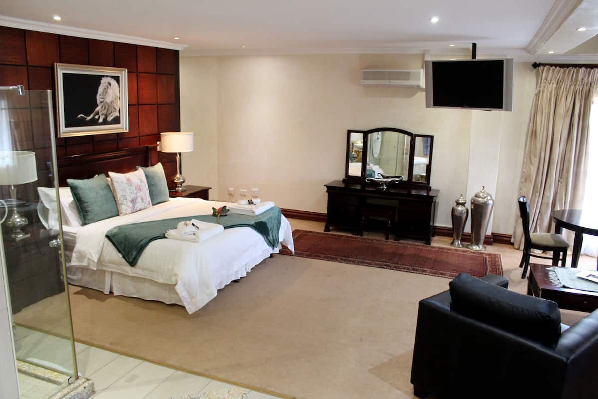 A hotel room with a bed, a desk, a TV, and a seating area.