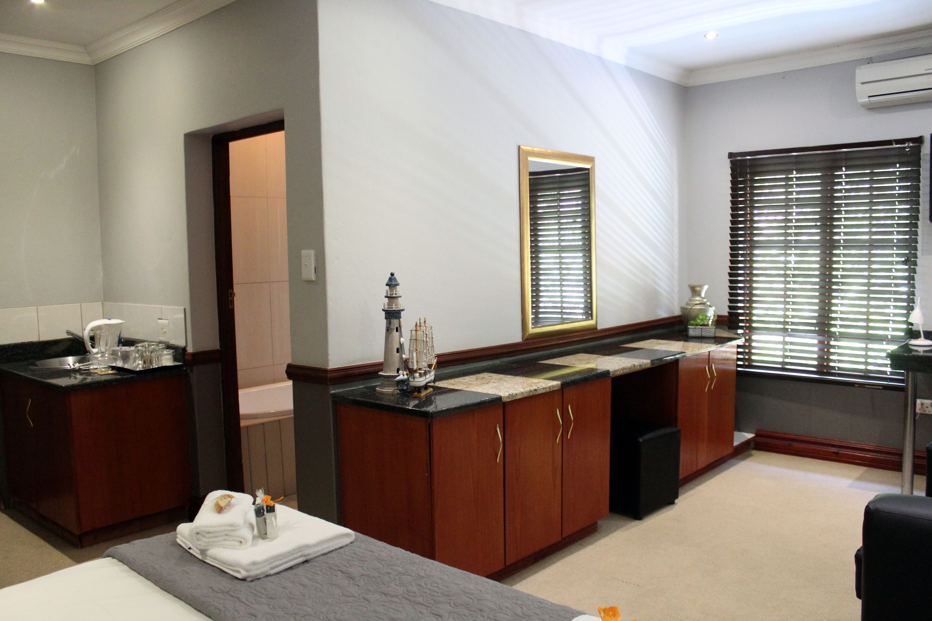 Habitación de hotel con cama, baño con lavabo y espejo, y ventana con persianas.