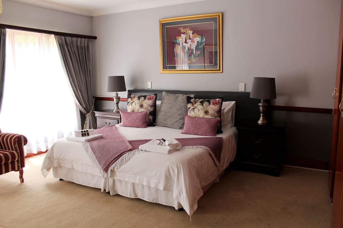 A neatly arranged bedroom with a large bed, two bedside tables with lamps, a chair, and a painting on the wall.
