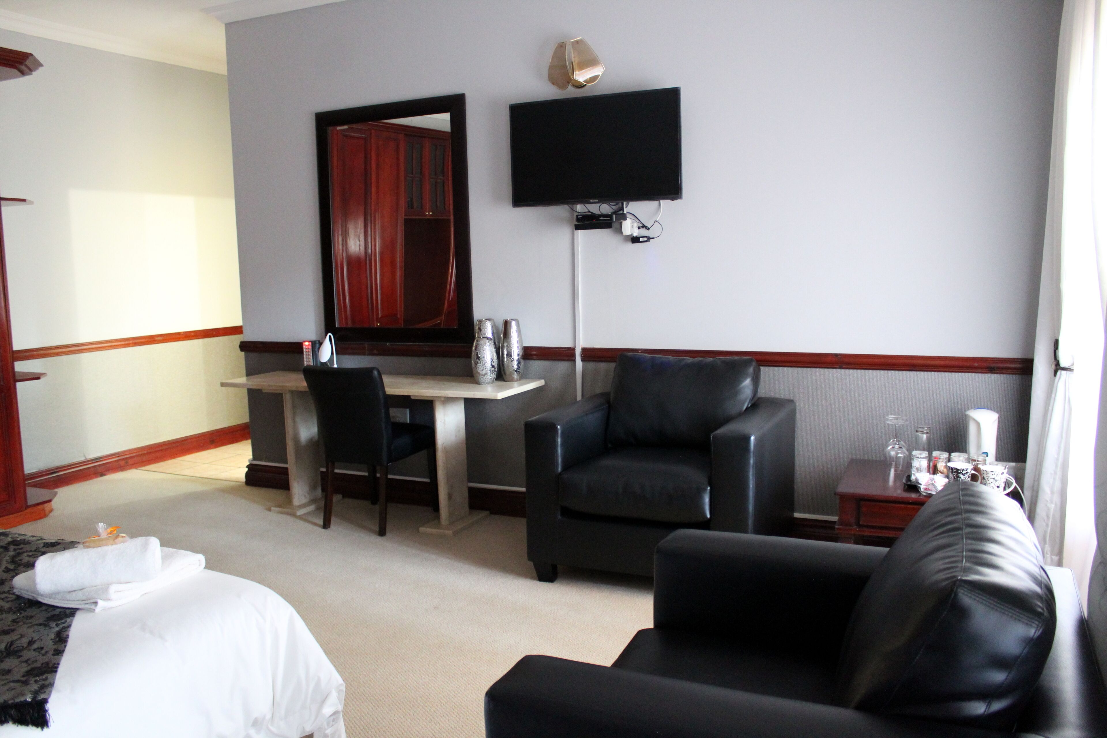 A hotel room with a bed, a desk, two chairs, a TV, and a small table with a lamp.