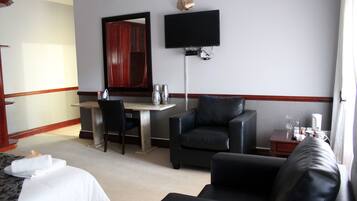Habitación de hotel con cama, escritorio, dos sillas, televisor y una pequeña mesa con lámpara.