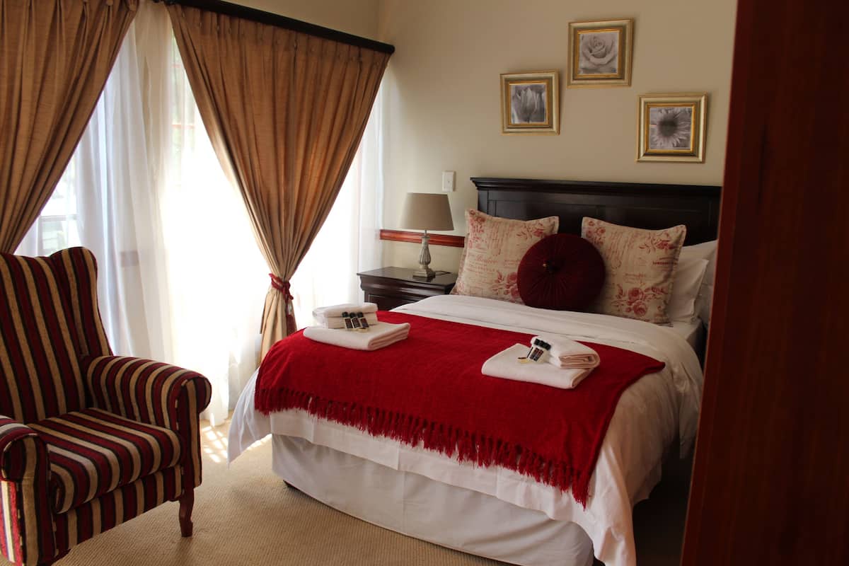 A hotel room with a large bed, a striped armchair, a nightstand with a lamp, and three framed pictures on the wall.
