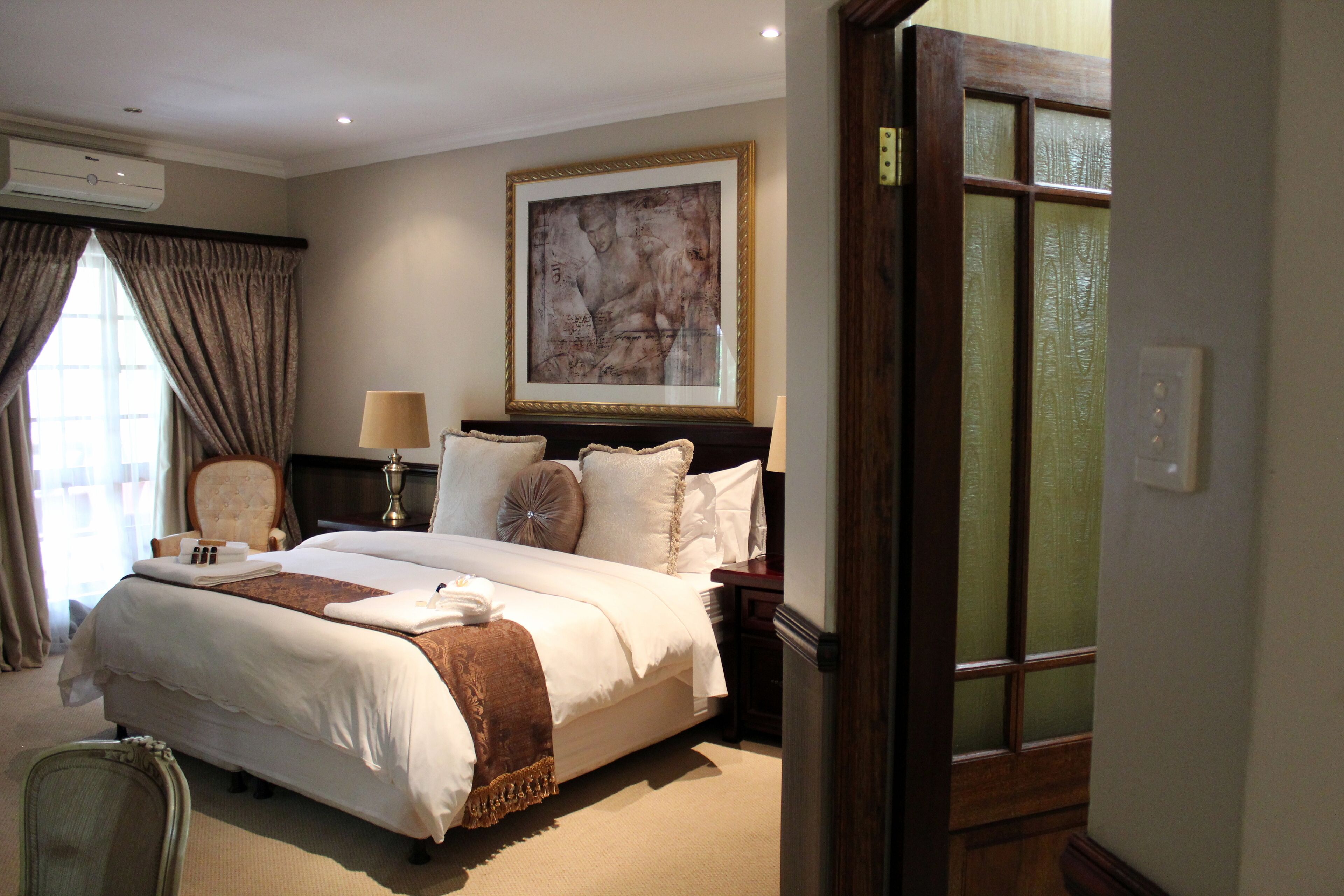Habitación de hotel con una cama grande, una silla, un cuadro en la pared y una ventana con cortinas.