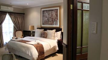 Habitación de hotel con una cama grande, una silla, un cuadro en la pared y una ventana con cortinas.